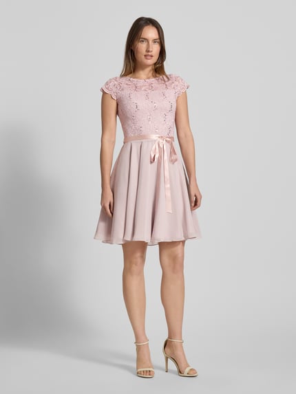 Vrouwenmodel draagt Cocktailkleid mit Spitzenbesatz und Bindegürtel van SWING, lichtroze, A-lijn minijurk met pailletten, tailleceintuur, mix van materialen met stretch. Volledige lichaamsaanzicht van voren.