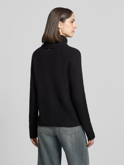 Männermodel trägt Regular Fit Pullover aus Alpaka-Woll-Mix Modell 'Falodina' von BOSS Orange, unifarben, Strickoptik, Rollkragen, raglanowe rękawy, długi rękaw, widok całej sylwetki z tyłu.