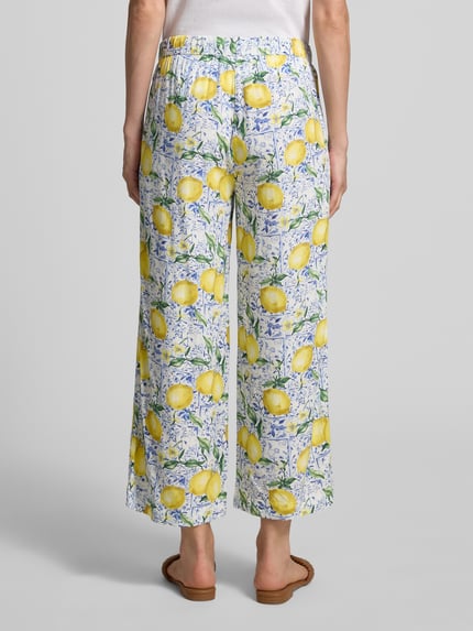 Vrouwenmodel draagt Caprihose aus Viskose im Allover-Look van Christian Berg Woman, zuiver viscose, relaxed fit, all-over look, elastische band, bandwijdte maat 36: 40 cm, binnenbeenlengte maat 36: 63 cm, kleurrijk citroenmotief, lichte stoffen textuur. Volledige lichaamsweergave van achteren.