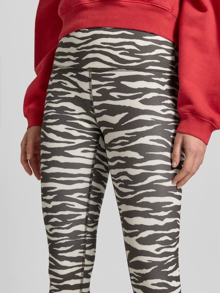 Kobieta nosi legginsy z dodatkiem streczu od Juvia, mieszanka materiałów, krój skinny fit, szeroki elastyczny pas, długość do kostek, Długość wewnętrzna nogawki 65 cm, szerokość w rozmiarze S 34 cm, wzór w czarno-białe pasy, zbliżenie na dolną połowę ciała, KI-modifiziertes Bild
