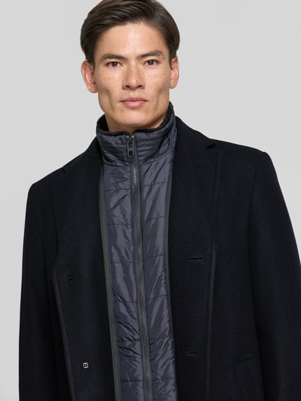 Männermodel trägt Regular Fit Mantel aus Woll-Mix von HECHTER PARIS in Schwarz, Reverskragen, glatte Textur, Nahaufnahme Oberkörper. Rückenlänge 95 cm, Schulterbreite 43 cm, Brustweite 57 cm, Ärmellänge 67 cm.