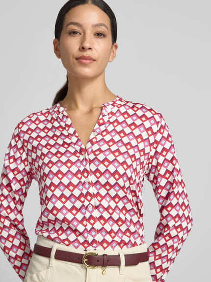 Frauenmodel trägt Bluse aus reiner Viskose von Emily Van den Bergh mit taillierter Passform und Knopfleiste, geometrisches Muster in Weiß, Rot und Violett, Langarm-Design; Nahaufnahme Oberkörper.