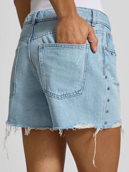 Frauenmodel trägt Regular Fit Jeansshorts aus reiner Baumwolle von REVIEW im Destroyed-Look, hellblaue Waschung, Nietenbesatz, Nahaufnahme Rückansicht.