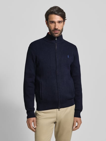 Męski model nosi Kardigan rozpinany z bawełny od Polo Ralph Lauren, krój regular fit, prążkowane wykończenia, stójka, wpuszczane kieszenie, wyhaftowane logo, zamek błyskawiczny, kolor granatowy, długość tyłu 70 cm, długość rękawów 65 cm, całkowity widok z przodu.