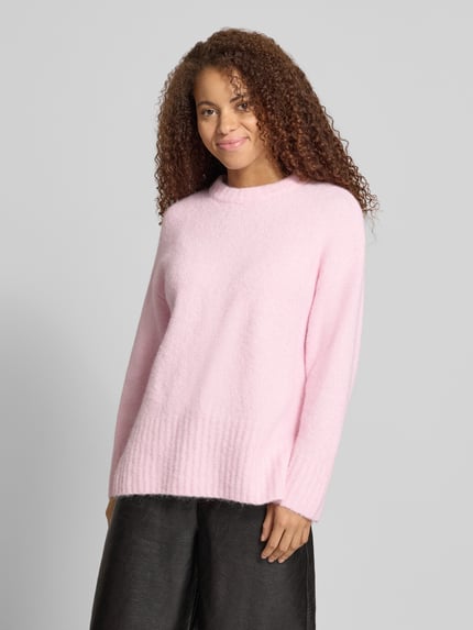 Modelka nosi sweter z okrągłym dekoltem PIECES 'Pullover mit gerippten Abschlüssen', jednokolorowy, krój regular fit, długi rękaw, wykończenie i rękawy prążkowane, długi fason, widok całej sylwetki z przodu.