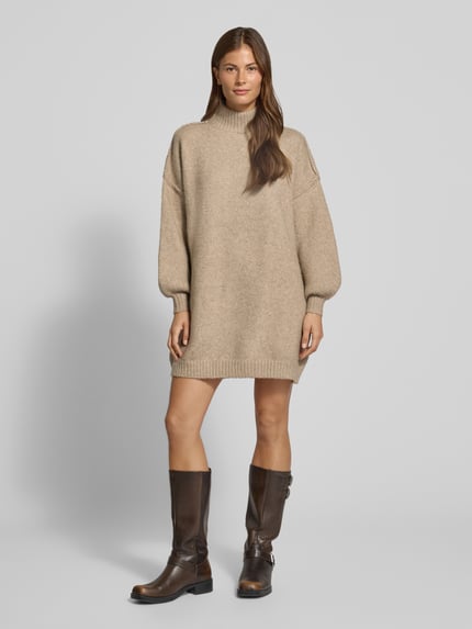 Frauenmodel trägt Strickkleid mit Stehkragen und überschnittenen Schultern von Apricot, beiges Minikleid aus Woll-Mix, gerader Schnitt, weiche Textur, Ganzkörperansicht von vorne. Rückenlänge 84 cm, Brustweite 62 cm, Ärmellänge 46 cm.