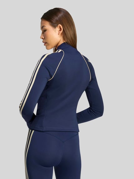 Frauenmodel trägt Slim Fit Trainingsjacke mit Zweiwege-Reißverschluss Modell 'OG SP MIDLAY' von adidas Training in Dunkelblau mit cremefarbenen Streifen, Ganzkörperansicht Rückansicht.