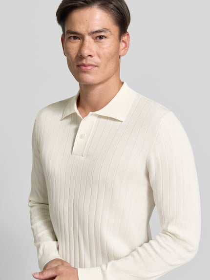 Mężczyzna nosi koszulkę polo Regular Fit z czystej bawełny model 'TORINO' od Selected, kremowy kolor, prążkowana faktura, zbliżenie na górną część ciała.