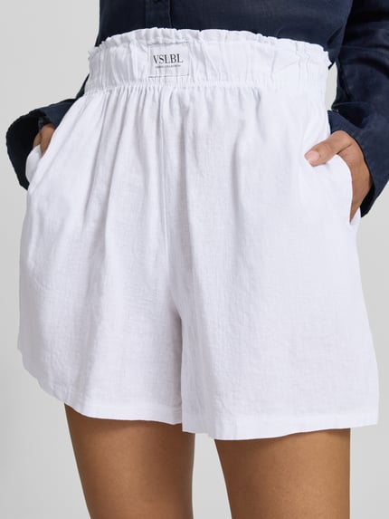 Frauenmodel trägt Regular Fit Stoffshorts aus Leinen-Baumwoll-Mix Modell 'MILLIE' von VILLA SOPHIE in Weiß mit elastischem Bund und Eingrifftaschen, Nahaufnahme Oberkörper, Fokus auf Textur und Allover-Muster.