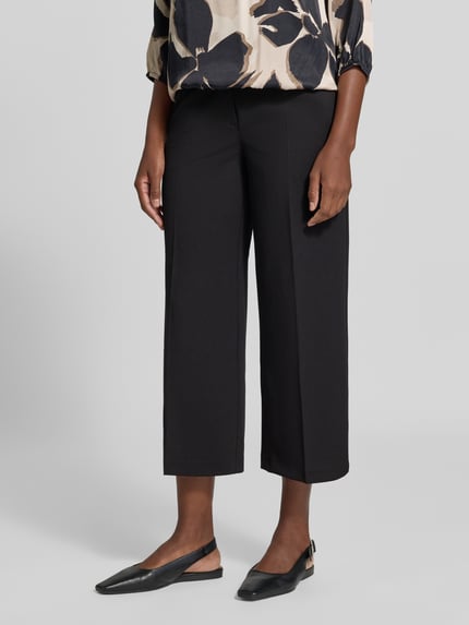 Frauenmodel trägt Regular Fit Weite Hose mit Bügelfalten Modell 'LT JULI' von Betty Barclay, schwarze Stofftextur, Nahaufnahme Unterkörper, Damen Weite Hose von Betty Barclay.