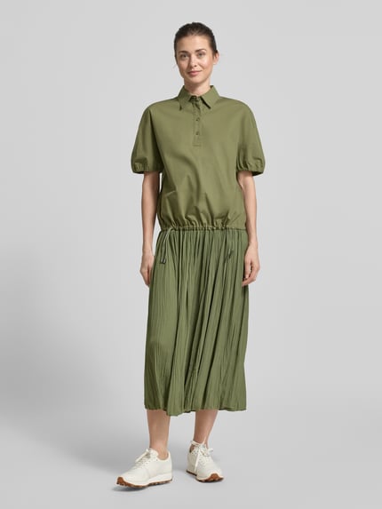 Frauenmodel trägt Regular Fit Bluse mit Polokragen von Marc Cain in Olivgrün, reine Baumwolle, elastische Ärmelabschlüsse, Bund mit Tunnelzug, ganzkörperansicht von vorne.
