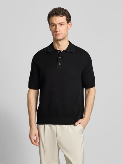 Männermodel trägt Relaxed Fit Poloshirt aus reiner Baumwolle Modell 'DANE' von SELECTED HOMME in Schwarz, Strickoptik, Ganzkörperansicht von vorne.