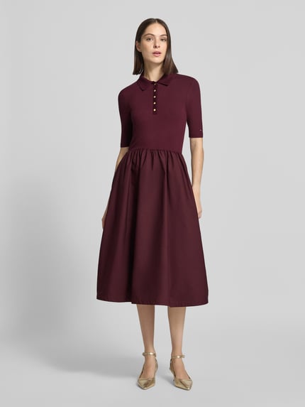 Frauenmodel trägt Midikleid mit Polokragen von Tommy Hilfiger in dunklem Bordeauxrot, leicht strukturierte Oberfläche, Ganzkörperansicht von vorne.