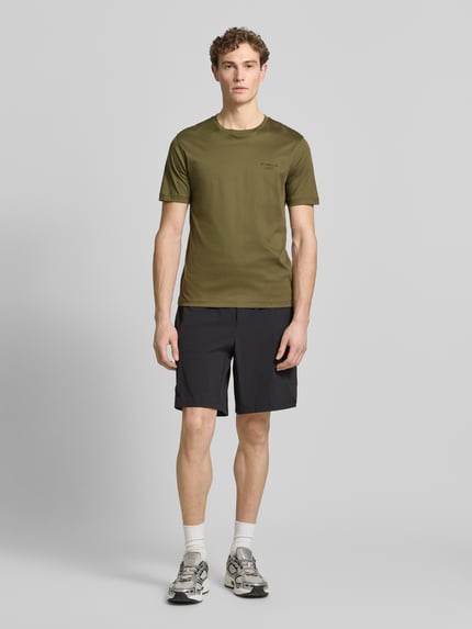 Männermodel trägt Regular Fit T-Shirt aus reiner Baumwolle Modell 'PS Spirit 70 Grx' von BOSS Green X PORSCHE in Olivgrün, unifarben, Rundhals, kurzarm, Ganzkörperansicht von vorne.