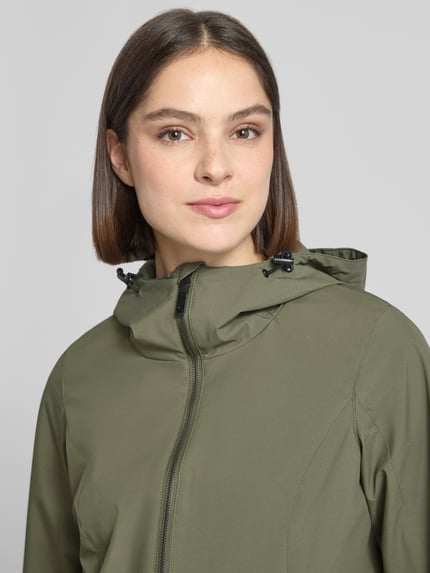 Frauenmodel trägt Regular Fit Regenmantel mit Logo-Detail von G.I.G.A. DX in Olivgrün, glatte Oberfläche, Nahaufnahme Oberkörper. Rückenlänge 76 cm, Schulterbreite 40 cm, Brustweite 50 cm, Ärmellänge 66 cm, Kapuze mit Tunnelzug, Zweiwege-Reißverschluss, Eingrifftaschen mit Reißverschluss.