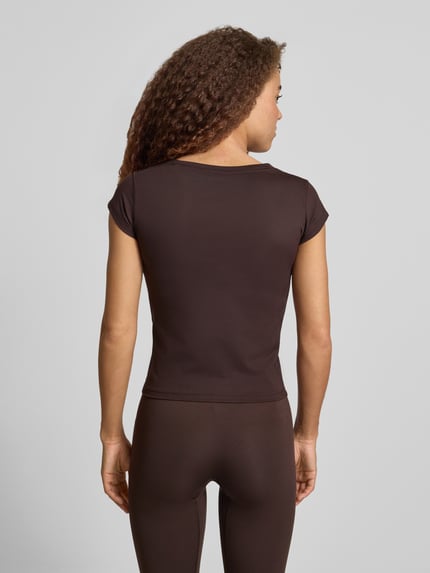 Kobiece model prezentuje Slim Fit Sport T-Shirt mit Label Print od adidas Sportswear, brązowy kolor, krój slim fit, struktura stretch, widok całej sylwetki z tyłu.