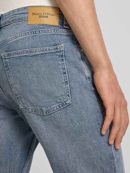 Männermodel trägt Tapered Fit Jeans aus Baumwoll-Mix von Marc O'Polo Denim in mittelblau mit sichtbarer Gesäßtasche, Nahaufnahme Rückansicht.