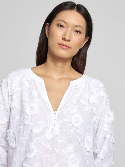 Frauenmodel trägt Regular Fit Bluse mit V-Ausschnitt und 3/4-Arm von Comma, weißer Material-Mix mit floralen Stitchings, Nahaufnahme Oberkörper. Rückenlänge bei Größe 36: 68 cm, Ärmellänge bei Größe 36: 57 cm.