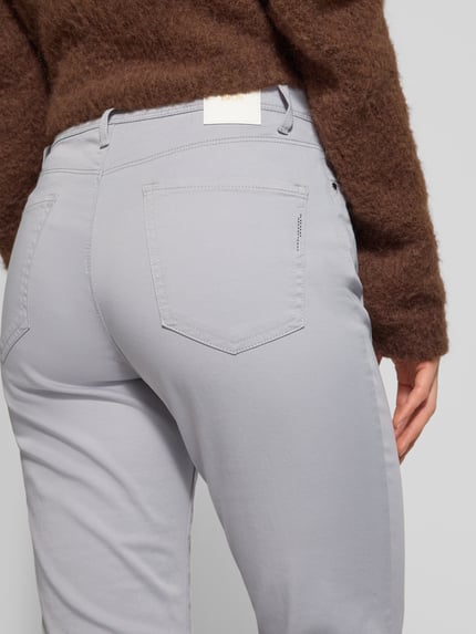 Frauenmodel trägt Flared Fit Jeans mit Lyocell-Anteil Modell 'Mary' von Brax in hellem Grau, 5-Pocket-Design, Nahaufnahme Rückansicht.