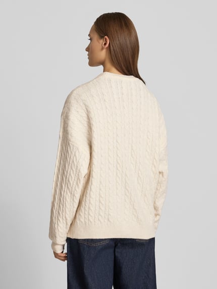 Frauenmodel trägt Oversized Fit Strickpullover mit Zopfmuster von REVIEW in Creme, elastischer Material-Mix, Rückenlänge 64 cm, Ganzkörperansicht Rückansicht.