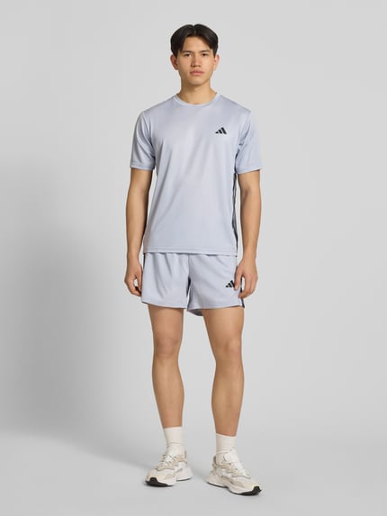 Männermodel trägt Regular Fit Sport T-Shirt mit Logo-Print von adidas Training in Hellgrau, unifarben, Mock-Eyelet-Gewebe, Ganzkörperansicht von vorne.