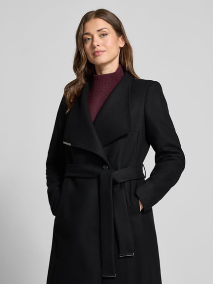 Vrouwenmodel draagt Mantel met Bindegürtel Modell 'ROSE' van Ted Baker in zwart, knoopsluiting, slim fit, opstaande kraag, labeldetail, taille met riem, effen oppervlak, borstbreedte 45 cm, mouwlengte 63 cm, schouderbreedte 40 cm, ruglengte 105 cm, close-up bovenlichaam.