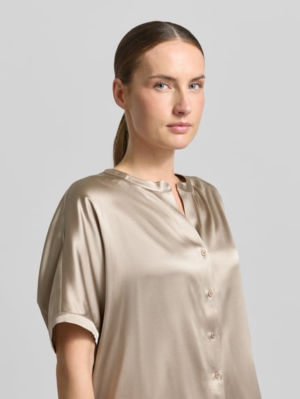 Vrouwenmodel draagt Relaxed Fit Seidenbluse mit Rundhalsausschnitt van HERZENS in zijdemix met knoopsluiting, korte mouwen, beige kleur, nahaufnahme bovenlichaam. Ruglengte maat 36: 63 cm, mouwlengte: 18 cm.