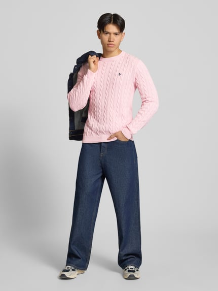 Männermodel trägt Strickpullover mit Zopfmuster und Logo-Stitching von REVIEW in Rosa aus Baumwoll-Mix, Modern Fit, Ganzkörperansicht von vorne.