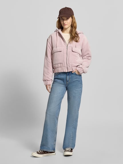 Frauenmodel trägt Regular Fit Bomberjacke mit Kapuze Modell 'SUVA' von ONLY aus Cord, Optik: unifarben, aufgesetzte Vordertaschen, Label-Stitching, gestreiftes Muster, elastischer Ärmel- und Rumpfabschluss, Reißverschluss, Ganzkörperansicht von vorne.