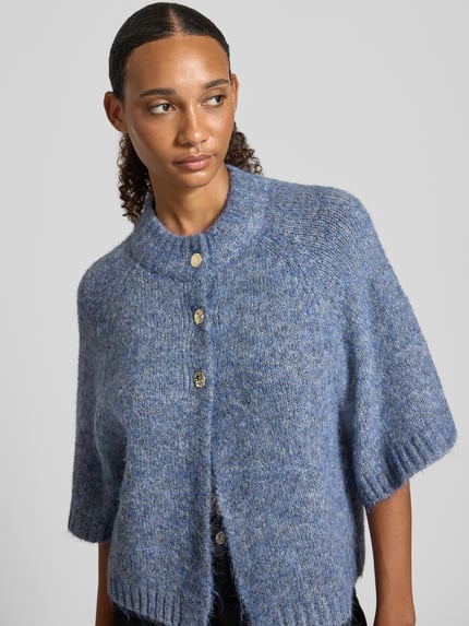 Kobiece model prezentuje kardigan Relaxed Fit Cardigan mit Woll-Anteil Model 'Benutta' od Neo Noir, elastyczna mieszanka materiałów z dodatkiem wełny, imitacja dzianiny, rękaw o dł. 1/2, listwa guzikowa, kolor niebieski melanż, widoczne miękkie tekstury, zdjęcie: zbliżenie na górną część ciała.