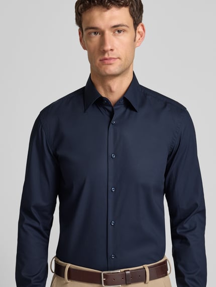 Męski model nosi Slim Fit Businesshemd aus Popeline mit Stretch-Anteil od BOSS, ciemnogranatowy, guzikami, bawełna-elastan, widok z przodu, z kontekstem: krój slim fit, kołnierz kent, pełny plisk, sportowe mankiety, zaokrąglony dół, easycare, długość pleców 76 cm, szerokość ramion 47 cm, długość rękawa 67 cm. Ganzkörperansicht von vorne.