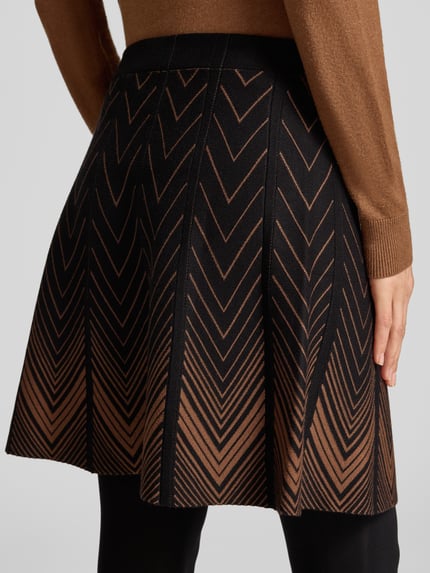 Frauenmodel trägt Strickrock im Allover-Look mit elastischem Bund von Apricot, braun-schwarze Viskose-Mix A-Linie, Minirock, Ganzkörperansicht Rückansicht.