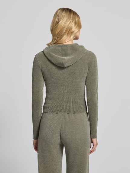 Frauenmodel trägt Sweatjacke mit Kapuze Modell 'MAYA KNIT HOODIE' von Juicy Couture in unifarbener, gestrickter Optik, cropped, Reißverschluss, Logo-Stitching, Kapuze, gerippte Abschlüsse, langarm, Ganzkörperansicht Rückansicht.