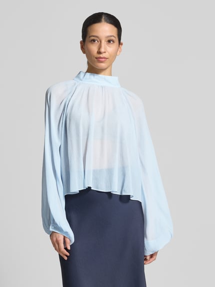 Modelka nosi Loose Fit Langarmbluse aus reiner Viskose Modell 'AFFETTO' od MAX&Co., efekt: jednolity kolor, krój relaxed fit, stójka, listwa guzikowa, długi rękaw, raglanowe bufiaste rękawy, mankiet, wykończenie materiału: crépon, materiał: czysta wiskoza, jasnoniebieska, lekko przezroczysta faktura, gładka powierzchnia, widoczne delikatne marszczenia. Ujęcie: całkowity widok z przodu.