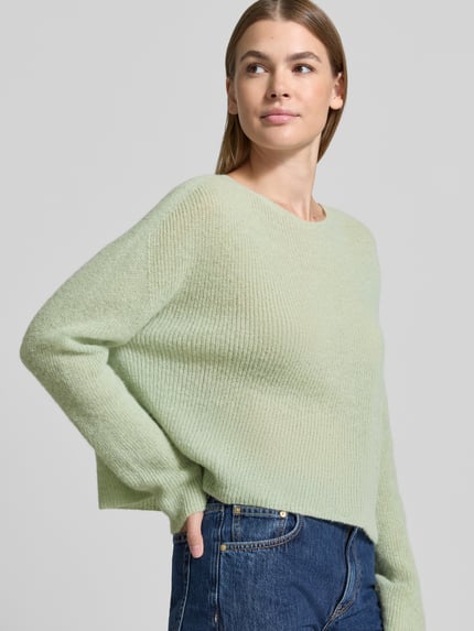 Vrouwenmodel draagt Oversized Wollpullover aus Alpaka-Mix van DRYKORN in lichtgroen, ribbeltextuur, ronde hals, wijde schouders, bovenlichaam close-up.