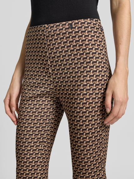 Kobieta nosi spodnie 'Flared Cut Hose im Allover-Look mit elastischem Bund' od Marc Cain, Mieszanka materiałów z dodatkiem streczu, rozkloszowany krój, wzór na całej powierzchni, elastyczny pas, szerokość w rozmiarze 36: 37 cm, długość wewnętrzna nogawki w rozmiarze 36: 82 cm, zbliżenie na górną część ciała