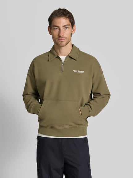 Männermodel trägt Regular Fit Troyer aus Baumwoll-Mix von Polo Ralph Lauren in Olivgrün mit Logo, glatte Textur, Ganzkörperansicht von vorne.