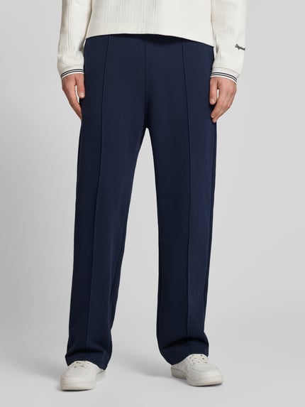 Männermodel trägt Sweatpants mit Längsnähten und Label-Stitching von CHAMPION in Dunkelblau, Baumwoll-Mix, Relaxed-Fit, Ganzkörperansicht von vorne.