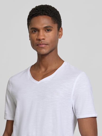 Männermodel trägt T-Shirt mit V-Ausschnitt und Rollsaum von MCNEAL, weiße Reine Baumwolle, Regular-Fit, Nahaufnahme Oberkörper.