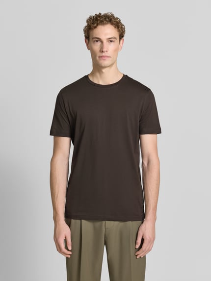Mężczyznamodel nosi T-Shirt aus Baumwolle mit Rundhalsausschnitt von Christian Berg Men, krój slim fit, okrągły dekolt, długość tyłu w rozmiarze M 73 cm, ciemnobrązowy kolor, prosta faktura, widok całej sylwetki z przodu.