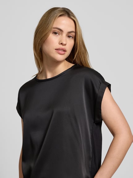 Frauenmodel trägt Blusenshirt mit fixierten Ärmelaufschlägen Modell 'VIELLETTE' von Vila, Viskose-Mix mit Stretch-Anteil, lockerer Schnitt, Rundhalsausschnitt, schwarze seidige Oberfläche, Nahaufnahme Oberkörper.