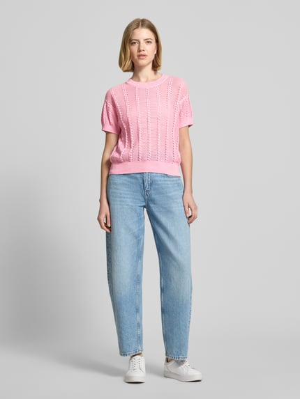 Modelka nosi Relaxed Fit Strick-Shirt aus Baumwoll-Mix Modell 'LUX LIGHT' od Vero Moda, różowy, ażurowy wzór, krótki rękaw, widok całej sylwetki z przodu.