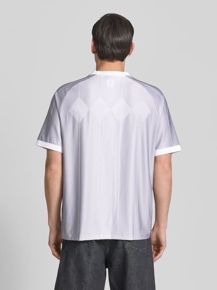 Mężczyznamodel nosi Regular Fit T-Shirt mit Label Print Modell 'DWILD' od HUGO, białe z całopowierzchniowym wzorem pasków i logo, krój regular fit, V-neck, krótkie rękawy z prążkowanym wykończeniem, Ganzkörperansicht Rückansicht.
