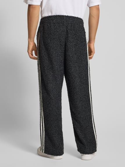 Männermodel trägt Sweatpants mit elastischem Bund van adidas Originals in bouclé-look, losse pasvorm, zwart met witte strepen, Ganzkörperansicht Rückansicht.