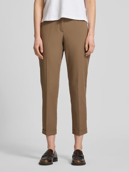 Vrouwenmodel draagt Chino uit Techno Cotton Superstretch model 'UTE' van Raffaello Rossi, straight fit, elastische mix met katoen, verkorte pasvorm, bruine kleur, persvouwen, steek- en achterzakken, knoop- en ritssluiting, vaste zoom, riemlussen. Vooraanzicht volledige lichaamsopname.