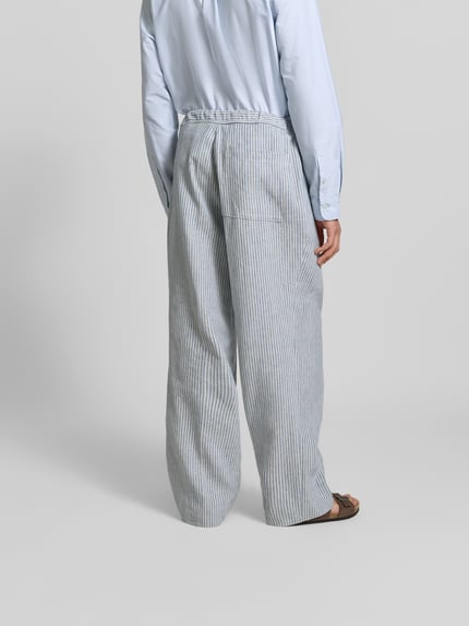 Mężczyzna nosi Wide Fit Stoffhose aus Leinen-Mix von Officine Générale, szare paski, elastyczny pas, kieszeń z tyłu, widok całej sylwetki z tyłu, długość nogawki 79 cm, szerokość w rozmiarze 50: 45 cm, tkanina z lnem i bawełną, kanty.