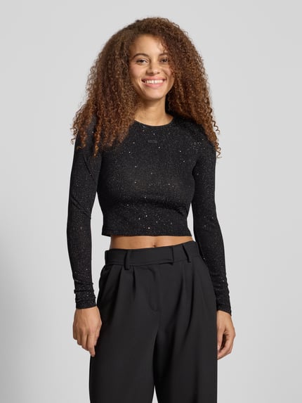 Frauenmodel trägt Cropped Longsleeve mit Label-Detail von Karo Kauer in Schwarz mit Glitter-Effekt, Regular Fit, Rundhalsausschnitt, Material-Mix mit Stretch, Ganzkörperansicht von vorne.