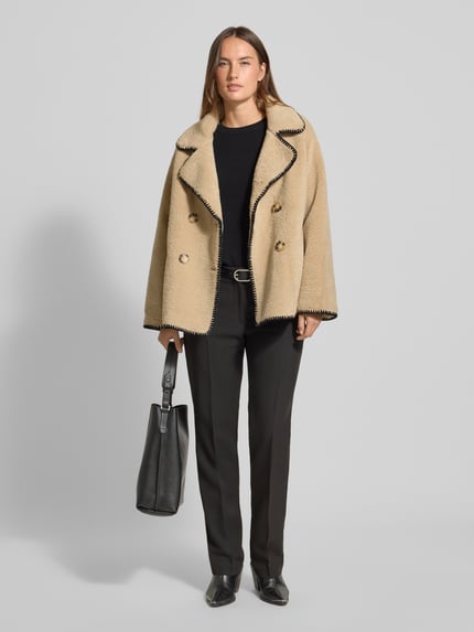 Frauenmodel trägt Jacke aus Teddyfell mit Eingrifftaschen von Apricot, relaxed Fit, zweireihig, beige mit schwarzem Reverskragen, Ganzkörperansicht von vorne.