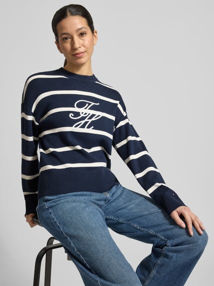 Frauenmodel trägt Regular Fit Sweatshirt aus reiner Baumwolle von Tommy Hilfiger im Allover-Streifenmuster mit Logo-Stitching, Feinstrick, Rundhals und langen Ärmeln, Farbton Dunkelblau mit weißen Streifen, Ganzkörperansicht von vorne.