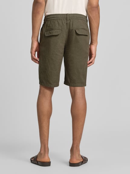 Männermodel trägt Bermudas aus Leinen-Mix mit französischen Eingrifftaschen von Lindbergh in Olive, Struktur sichtbar, Ganzkörperansicht Rückansicht, Leinen-Baumwoll-Mix, Straight Fit, elastischer Bund mit Kordelzug, Knopf- und Reißverschluss, Gesäßtaschen, Bundweite bei Größe M 43 cm, Innenbeinlänge 24 cm.